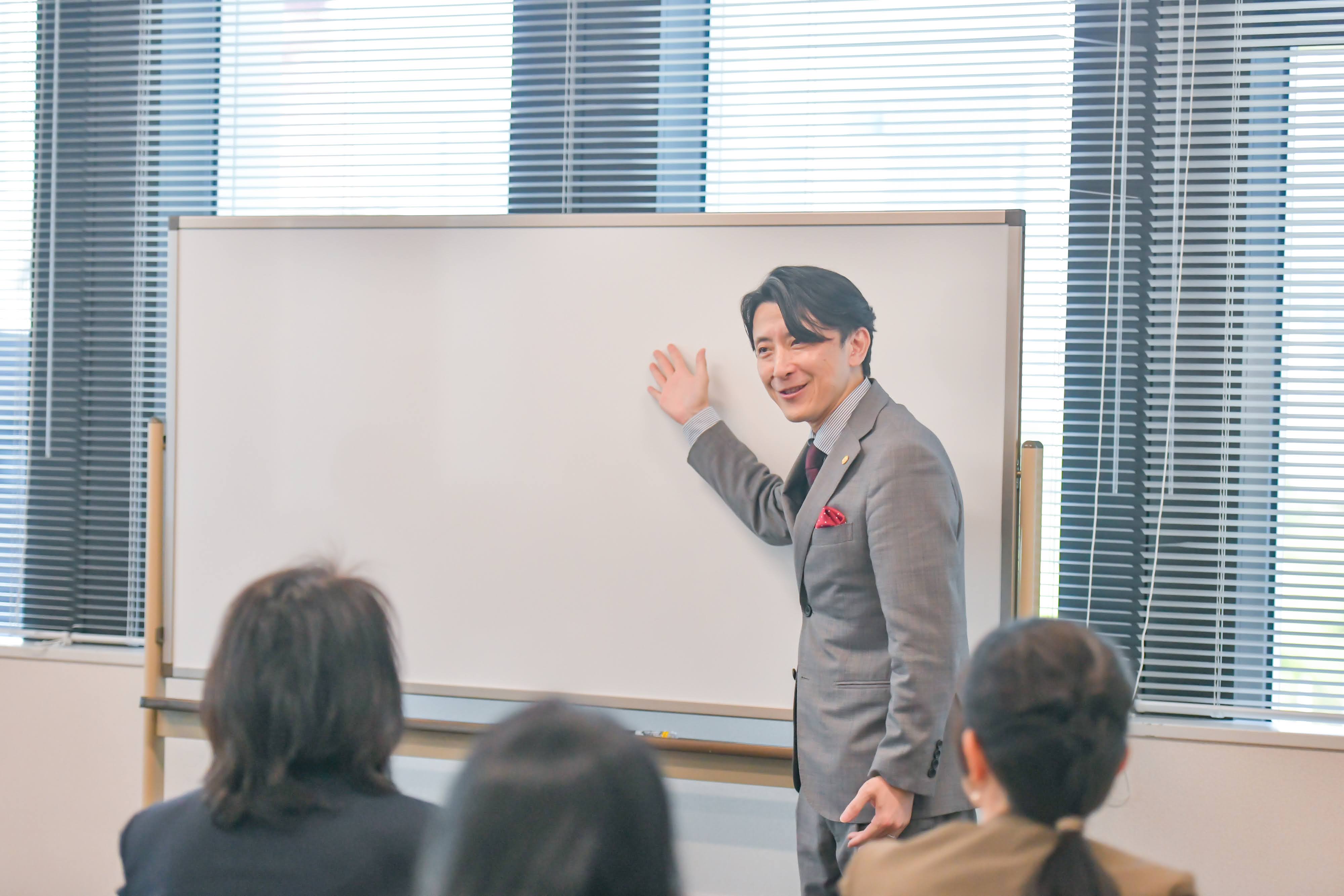 秋山康二郎がホワイトボードの前で研修を進める様子